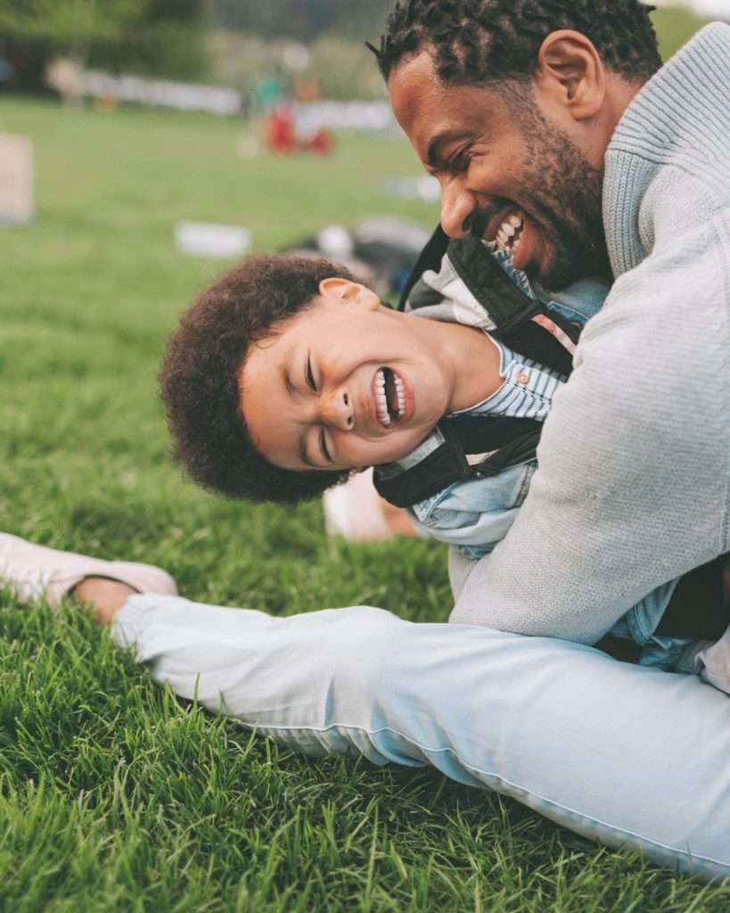 Father and son hugging and laughing in the park, reflecting the joy and family involvement crucial in speech therapy for toddlers.