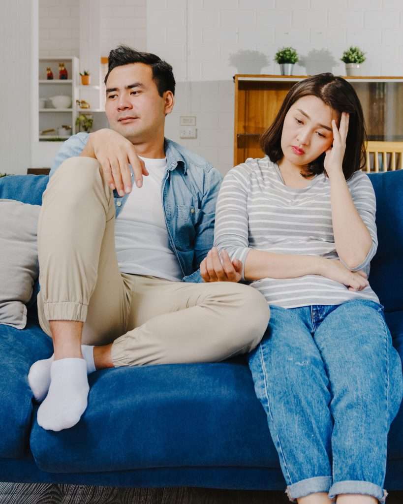 Concerned parents on sofa wondering, 'Did I cause my child's speech delay?' in a moment of reflection.