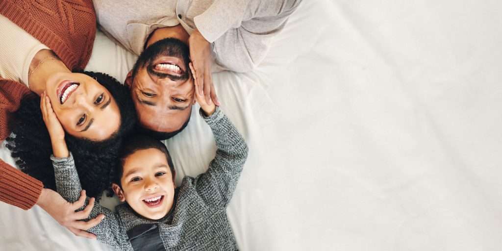 Family with toddler smiling on bed, enjoying success from Virtual Speech Therapy.