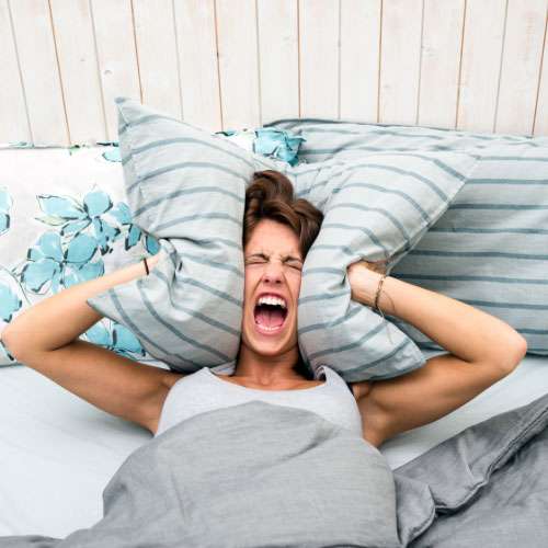 Woman in bed with pillow around ears, representing sleep issues associated with autism in women.