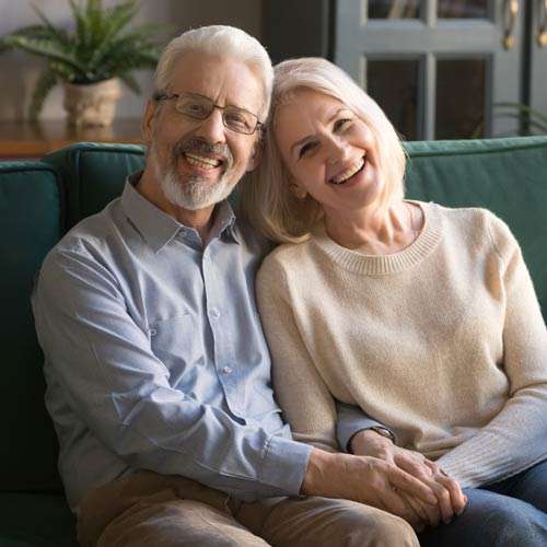 A couple in their home hugging and smiling on the sofa.