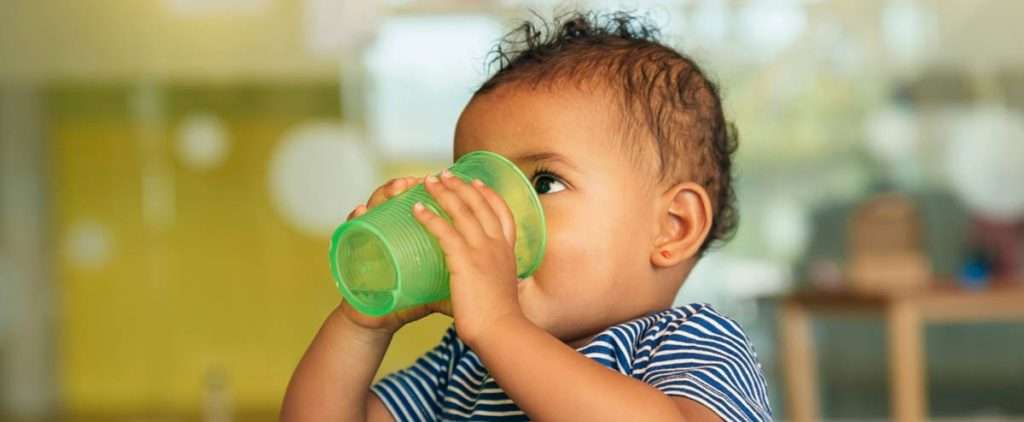 Infant drinking, while parents play games with her for language learning.
